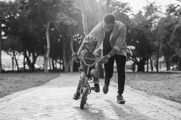 Ett barn lär sig cykla, en man springer bakom och håller i styret.