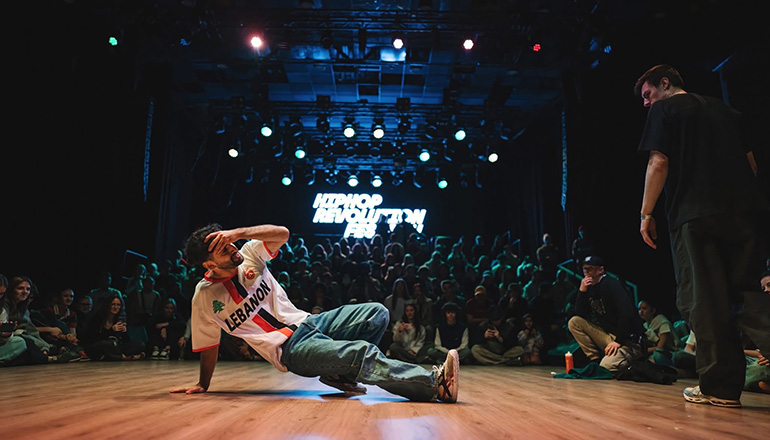 En man dansar breakdance med sittande publik intill.