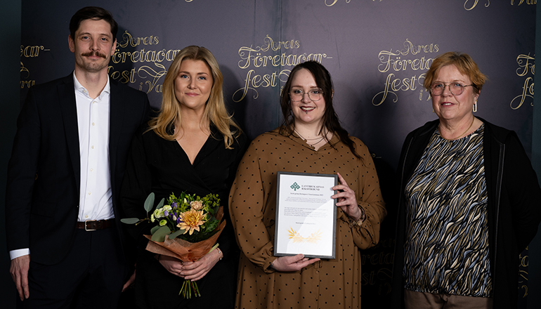 En man och tre kvinnor med blommor och diplom i händerna.