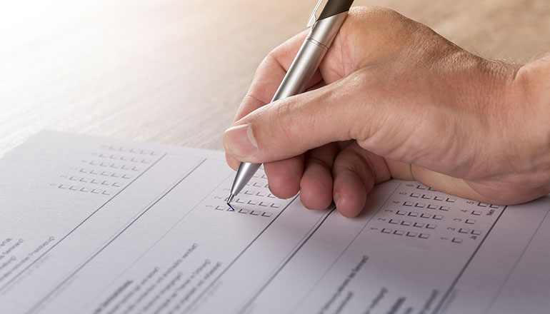 Närbild på en hand som håller i en penna och fyller i ett formulär.