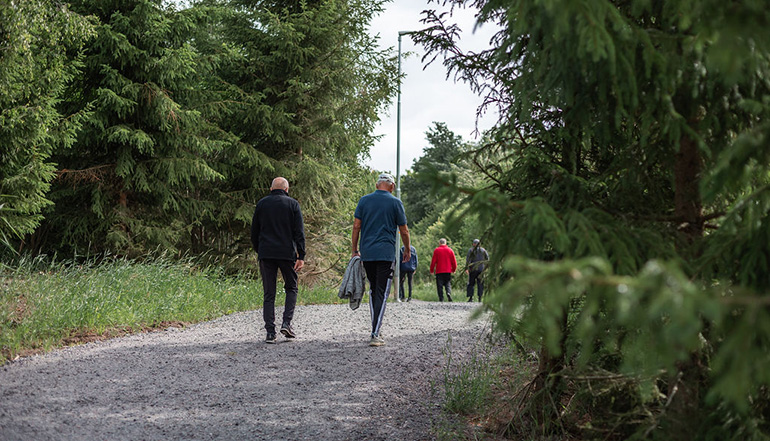 Fyra personer promenerar på en stig i en skog, fotograferat bakifrån.