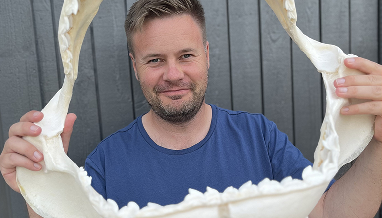 Man i t-shirt håller i ett stort skelett av en hajs käke.