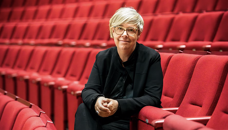 Karin Beckman sitter i en bänkrad med röda stolar på konsertläktare