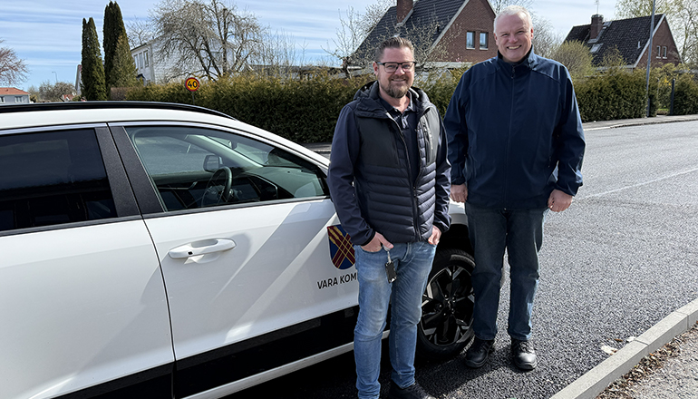 Två män står framför en vit bil.