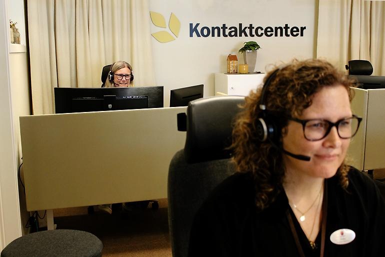 Två glada kvinnor arbetar i ett kontorslandskap. Båda har headset. På väggen står ordet "kontaktcenter".
