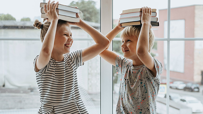 Två barn som balanserar böcker på sina huvuden.