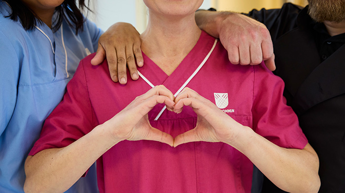 Närbild på tre personer i omvårdnadskläder, med händer som formar ett hjärta