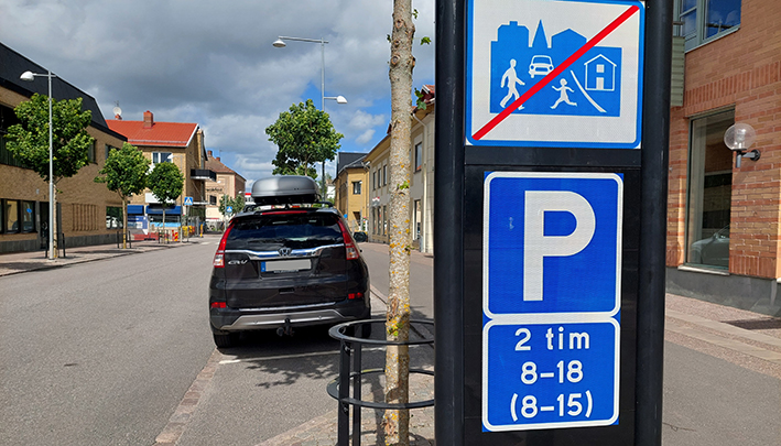 Till vänster finns en skylt med information om parkeringstider. Flera bilar står parkerade längs med gatan.