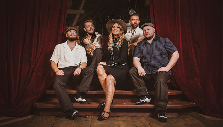 Fyra män och en kvinna i westerninspirerade kläder sitter i en trappa.