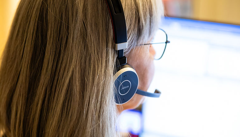 Kvinna med headset vid en dator, fotograferad bakifrån i närbild.