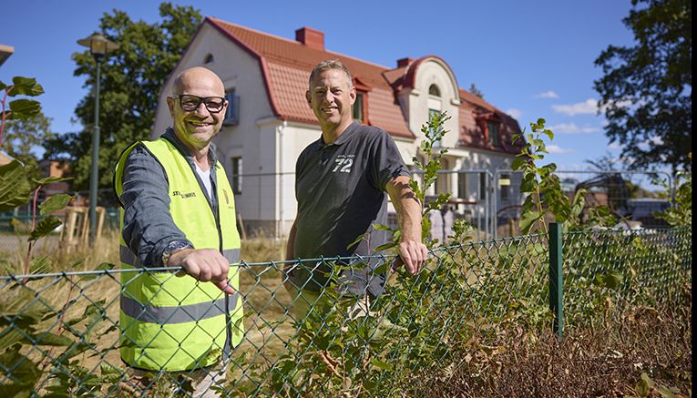 Två män står vid ett stängsel. I bakgrunden finns ett stort vitt hus som byggs om.