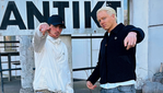Två unga män poserar framför en vägg med texten Antikt.
